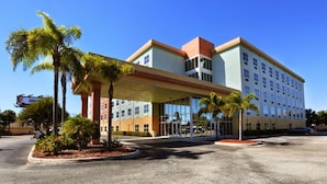 A multi-story hotel with a central atrium, palm trees, and a parking lot. - Allure Suites (Fort Myers)
