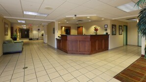 A reception area with a wooden desk, a green sofa, and a tiled floor. - Allure Suites (Fort Myers)