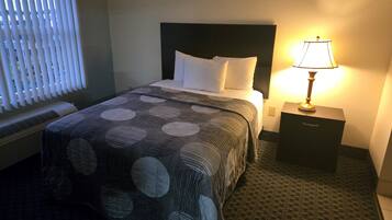Una camera d'albergo con un letto, un comodino, una lampada e una finestra con persiane.