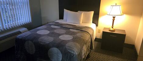 A hotel room with a bed, a nightstand, a lamp, and a window with blinds.
