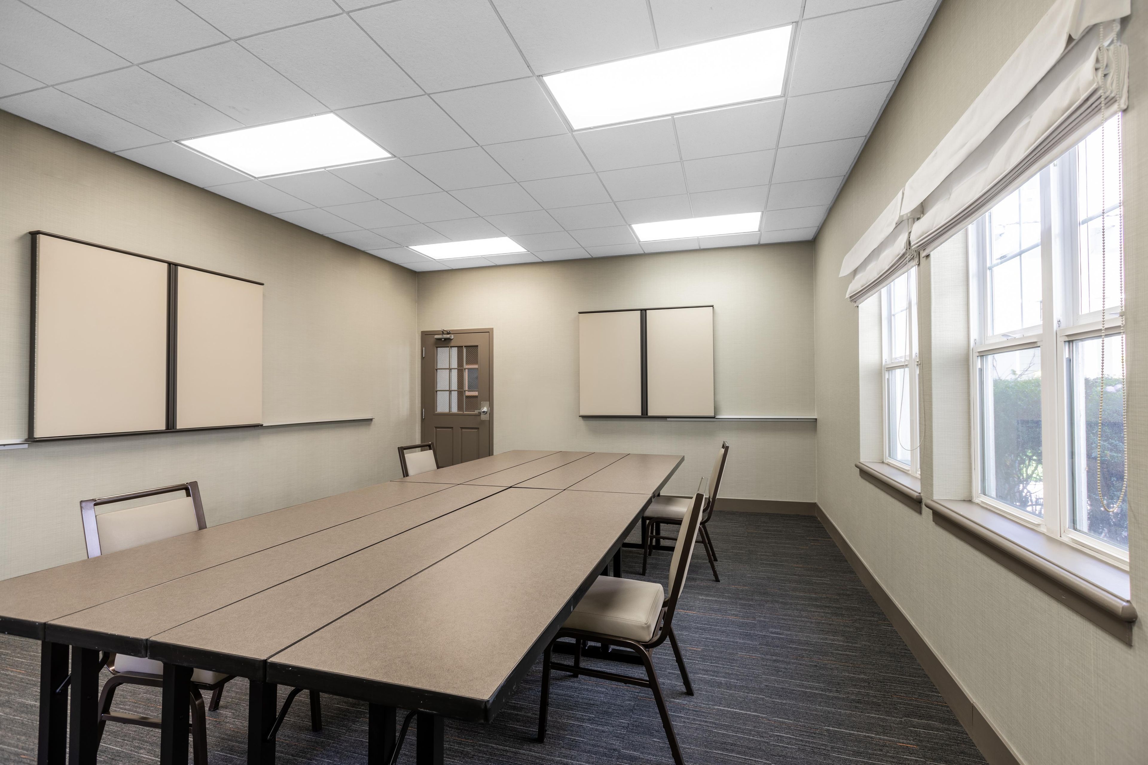 A conference room with a long table, chairs, a door, and windows.
