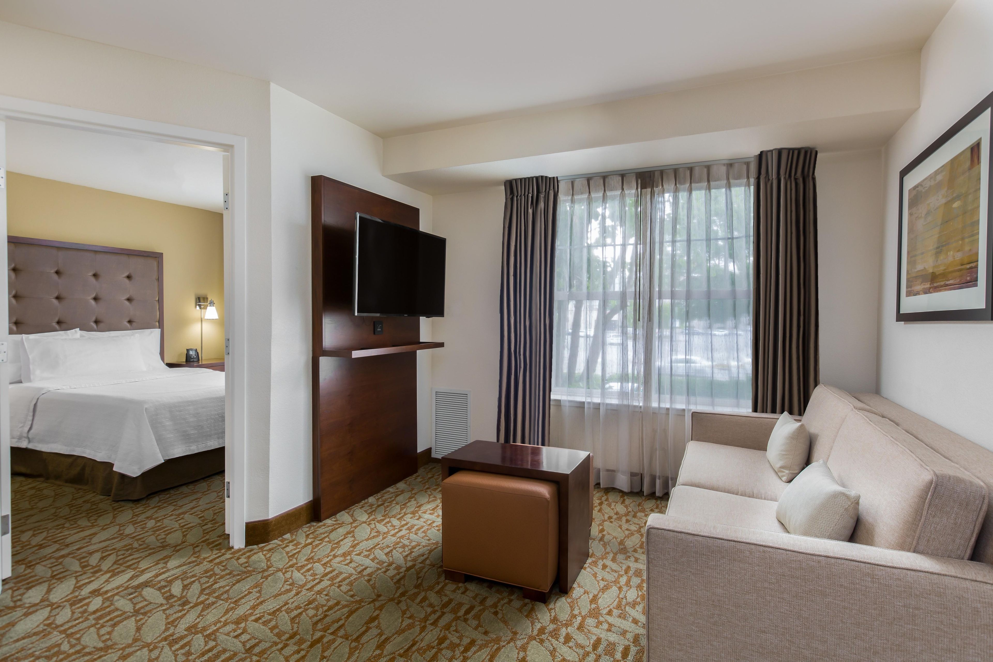 A hotel room with a bed, a sofa, a TV, and a window with curtains.