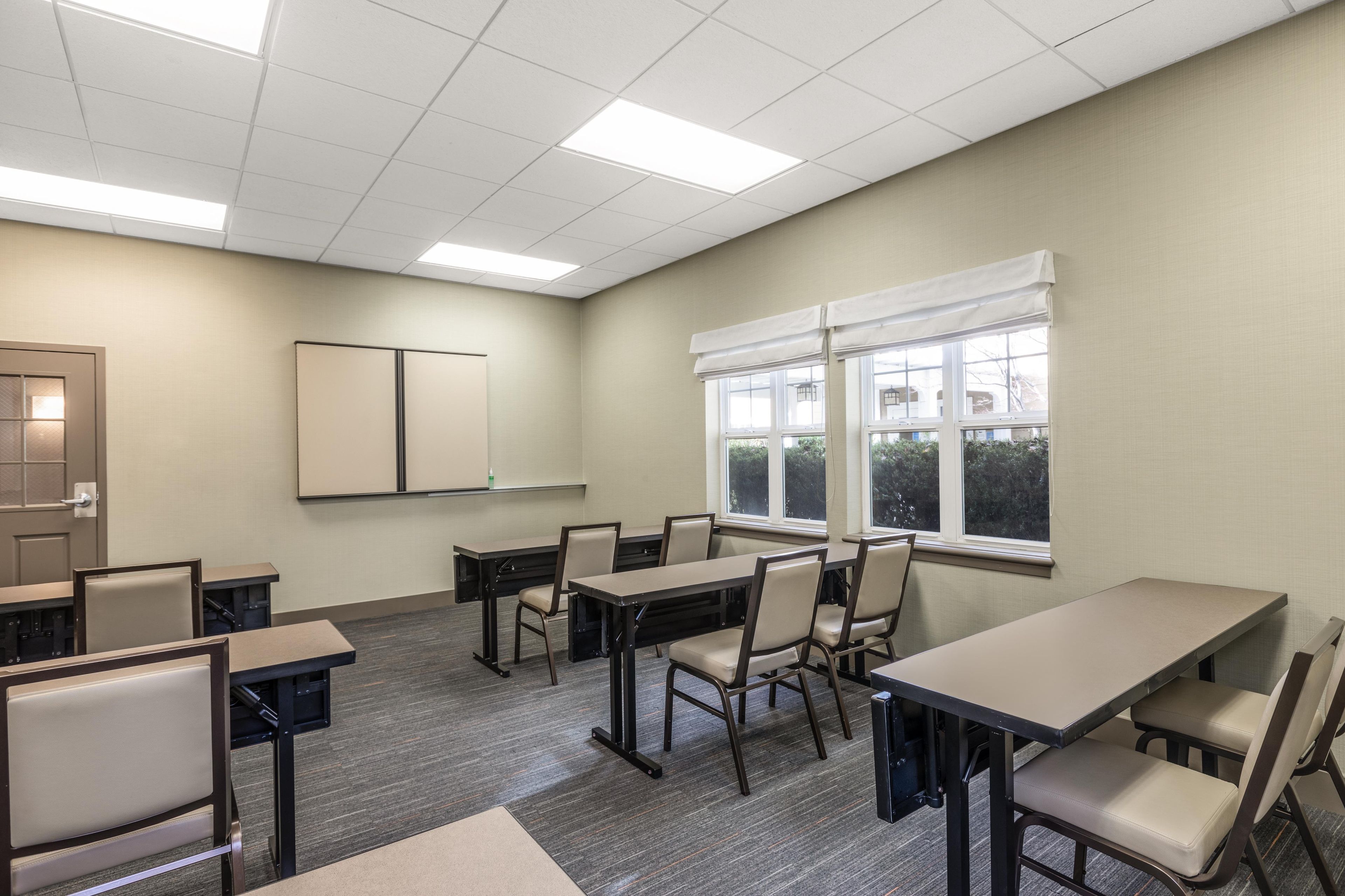 A conference room with tables and chairs, a whiteboard, and a window with blinds.