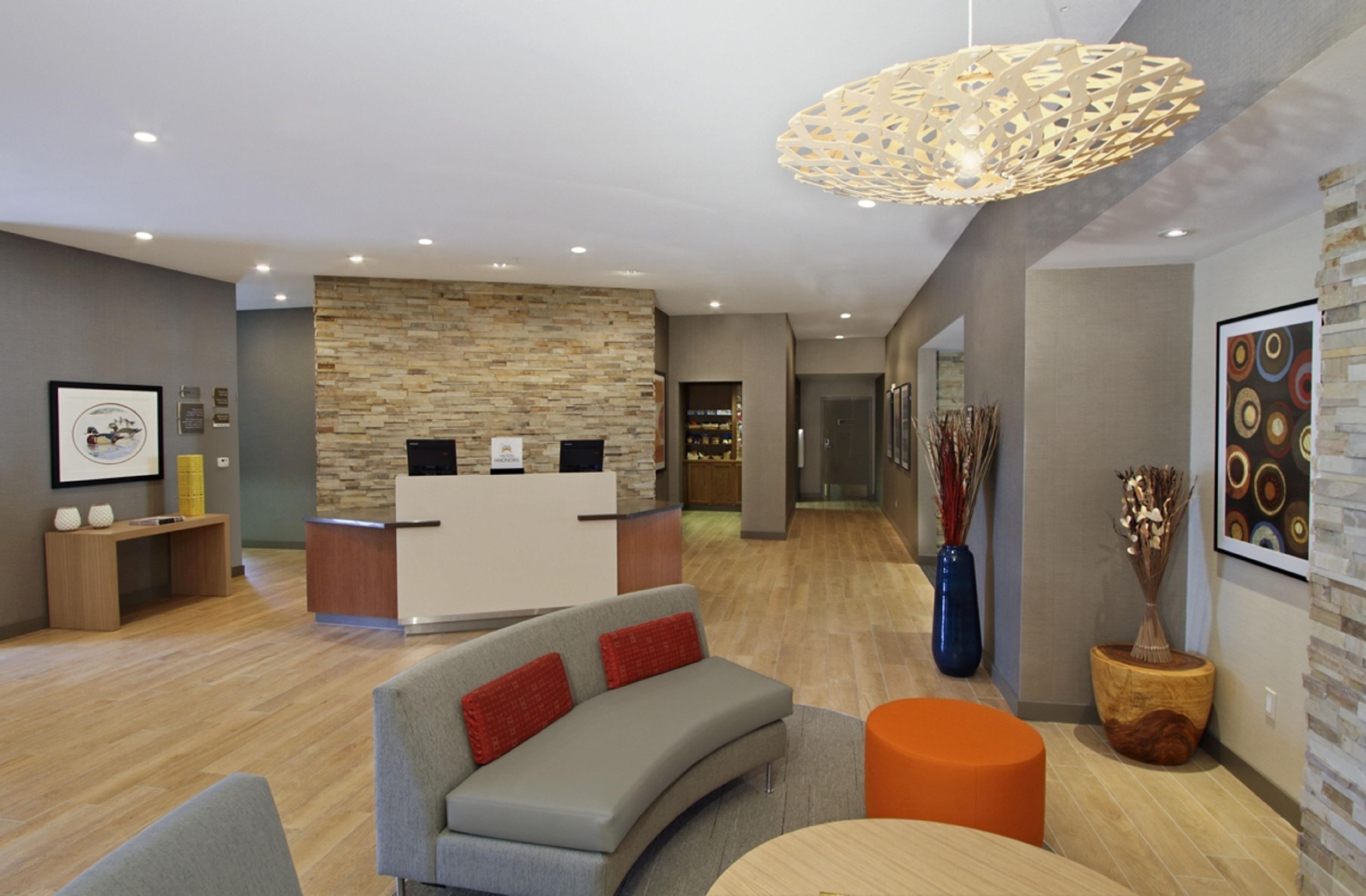 Un área de recepción moderna con pared de piedra, un mostrador y un espacio de espera con sofá y otoman.