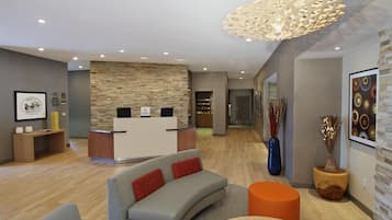 Ein moderner Empfangsbereich mit einer Steinwand, einem Empfangsschalter und einer Sitzecke mit Sofa und Hocker.