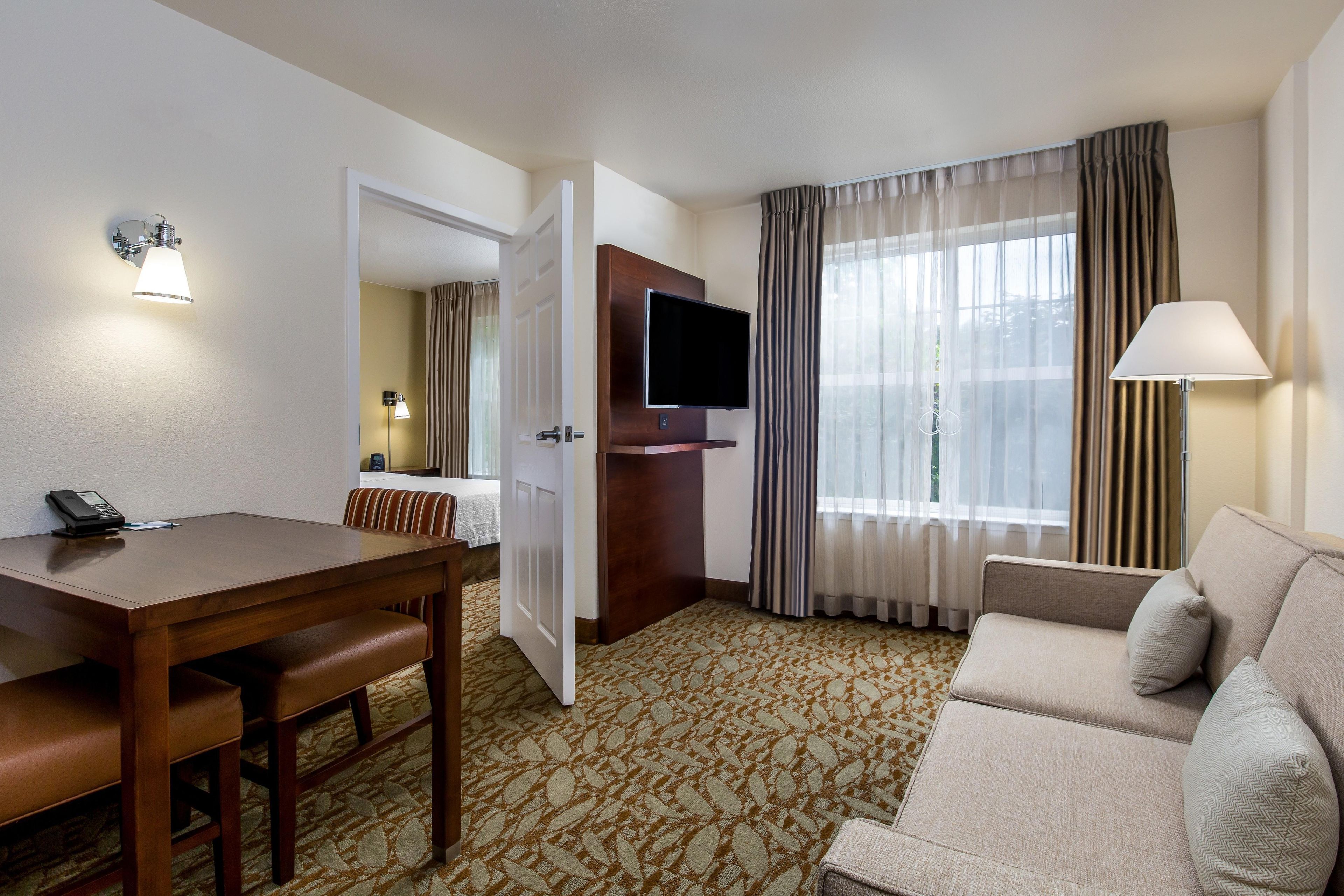 A hotel room with a dining table, a sofa, a TV, and a lamp.