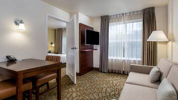 A hotel room with a dining table, a sofa, a TV, and a lamp.