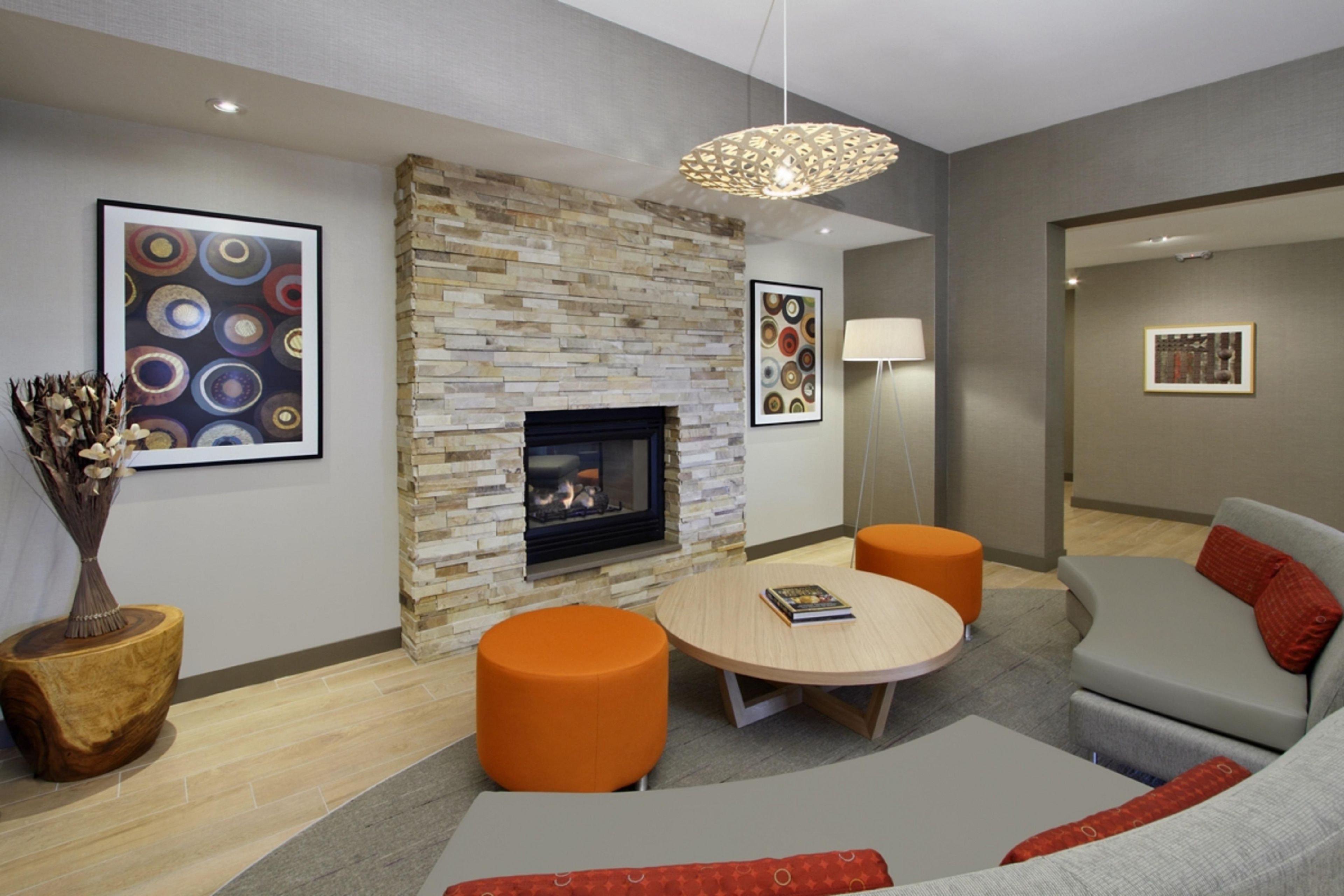 A modern living room with a stone fireplace, orange ottomans, a grey sofa, and abstract art on the walls.