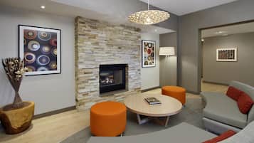 A modern living room with a stone fireplace, orange ottomans, a grey sofa, and abstract art on the walls.