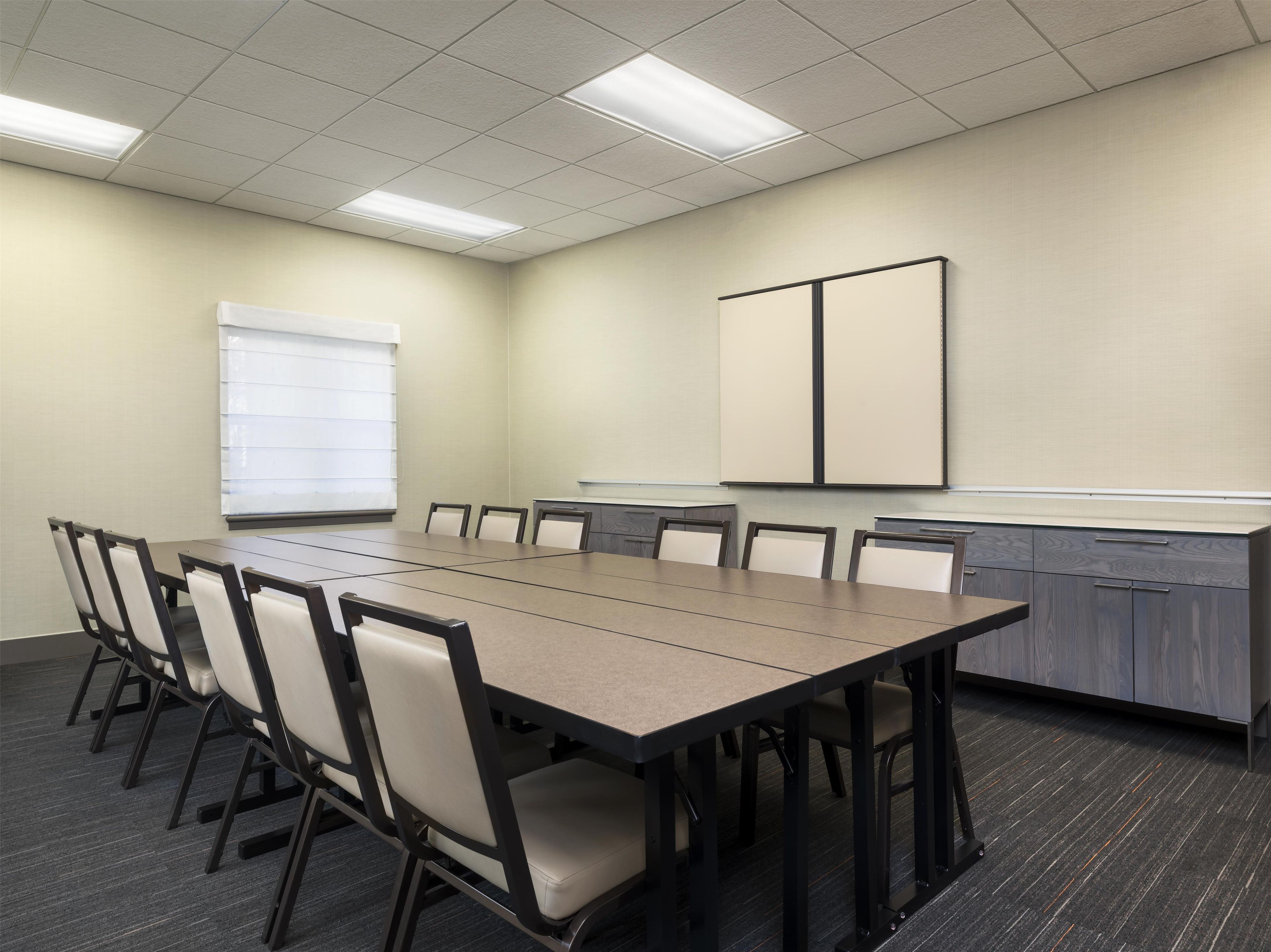 A conference room with a long table, chairs, a projector screen, and a whiteboard.