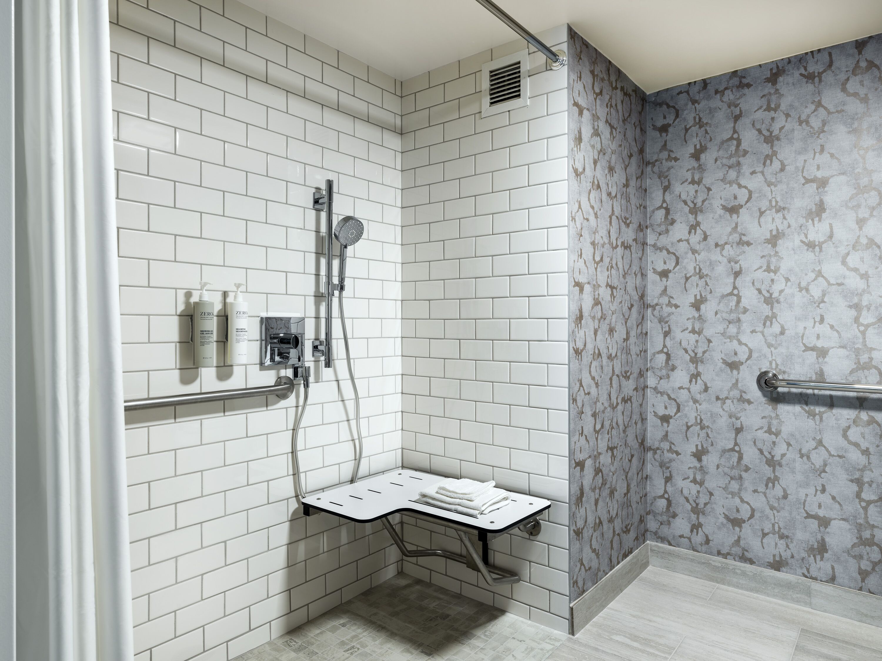 A modern bathroom with white subway tiles, a shower with a handheld showerhead, a towel rack, and a small shelf with toiletries.