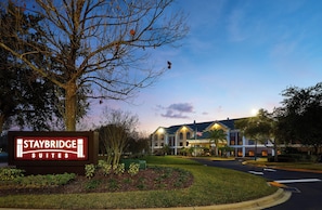 Een Staybridge Suites bord met een aangelegde tuin en een gebouw op de achtergrond.