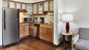 A compact kitchen with wooden cabinets, a stainless steel refrigerator, a microwave, a coffee maker, and a sink. - Staybridge Suites Orlando Airport South by IHG (Orlando)