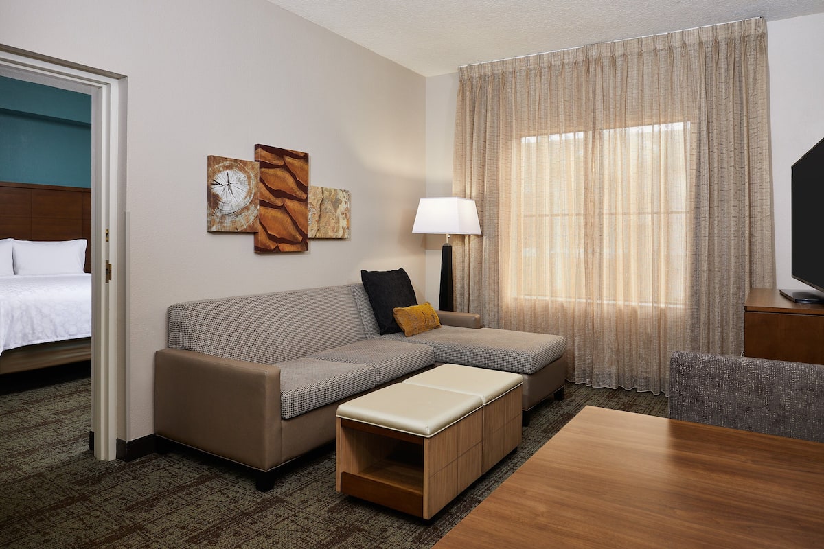 A hotel room with a bed, a sofa, a small table, a lamp, and a TV.