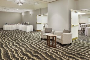 A hotel room with a patterned carpet, a seating area with a small table, and a buffet setup with food service equipment. - Staybridge Suites Orlando Airport South by IHG (Orlando)