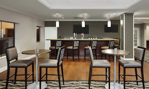A bar area with multiple stools, a bar counter, and a television mounted on the wall. - Staybridge Suites Orlando Airport South by IHG (Orlando)