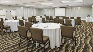 Un salón de conferencias con mesas redondas, sillas y una pantalla de proyector.