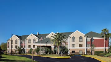 A multi-story hotel with a central courtyard, featuring a flagpole, palm trees, and a clear blue sky.