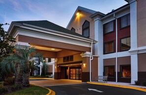 Entrada de un hotel con un paseo techado, un pilar de piedra y una banca.