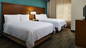 A hotel room with two beds, a wooden headboard, a nightstand with a lamp, a television on a wooden cabinet, and a large window with curtains. - Staybridge Suites Orlando Airport South by IHG (Orlando)