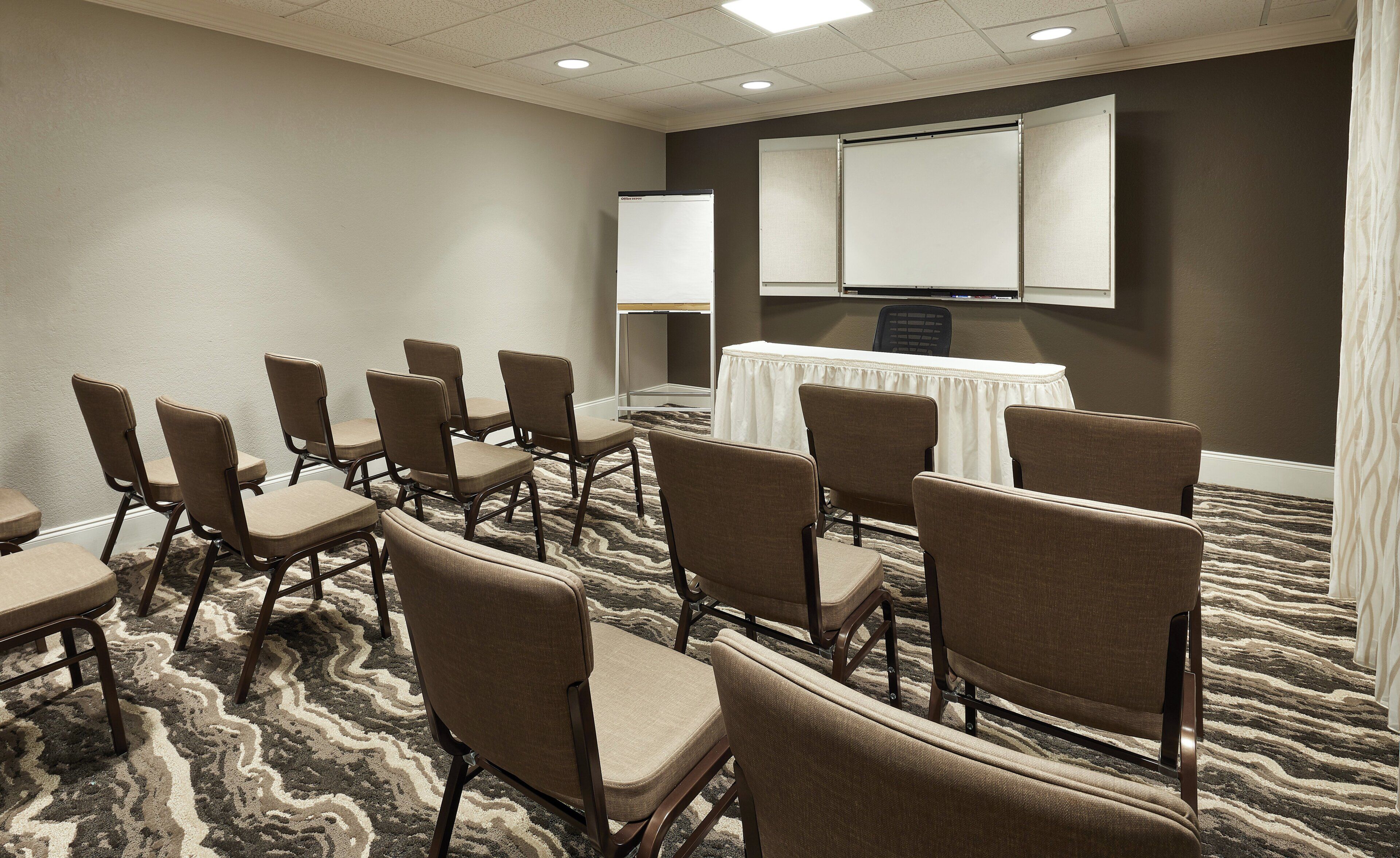 A conference room with a carpeted floor, a white table with a tablecloth, and several chairs arranged around it.