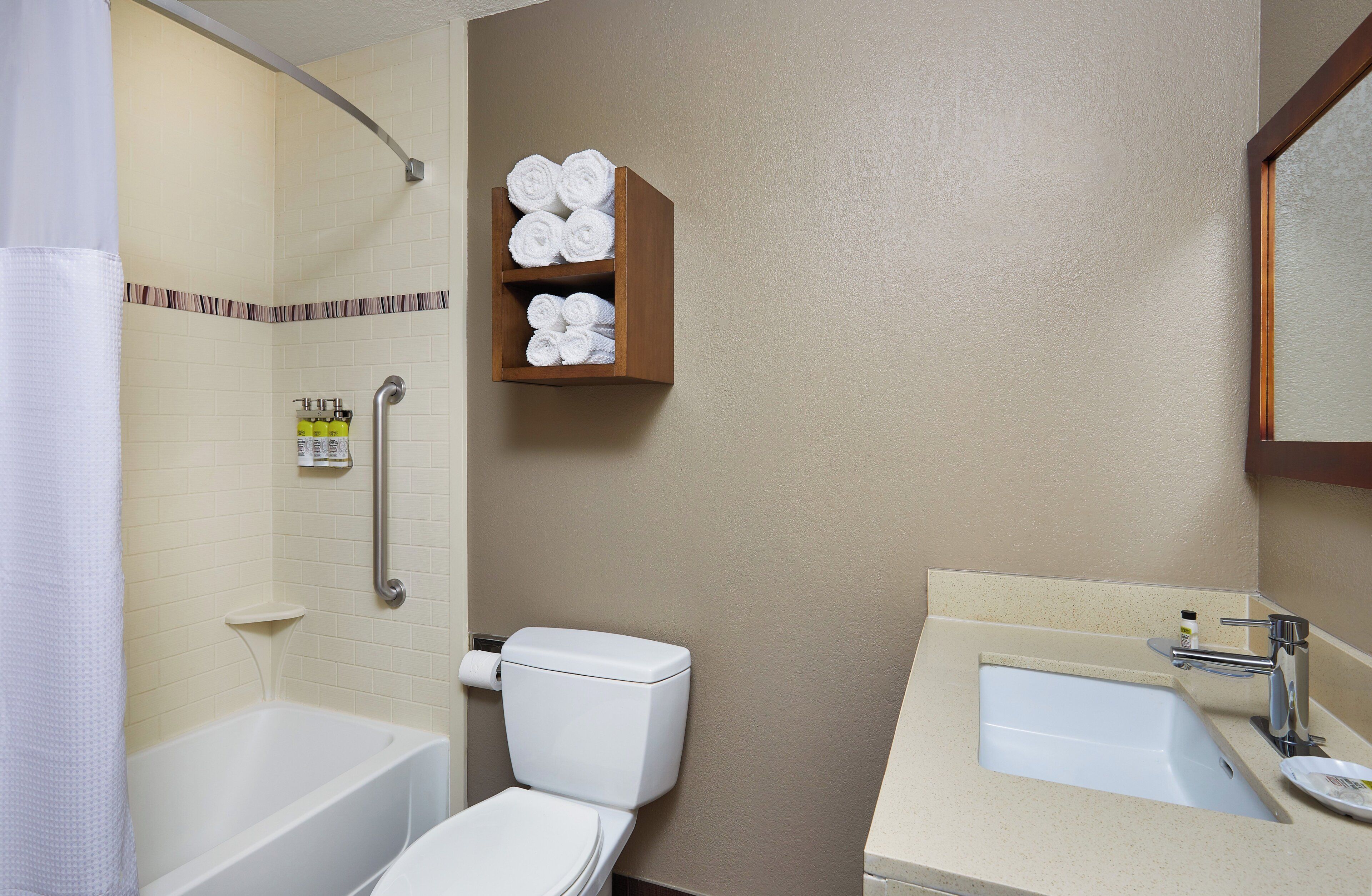 Une salle de bain avec une baignoire, des toilettes et un lavabo avec un miroir. On y trouve un porte-serviettes avec des serviettes et un rideau de douche.