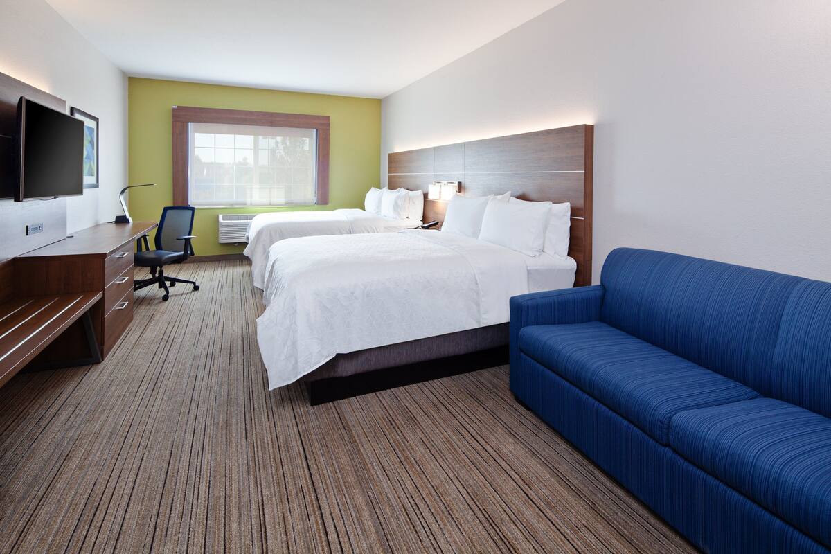 Une chambre d’hôtel avec deux lits, un bureau avec une chaise, une télévision et une grande fenêtre.