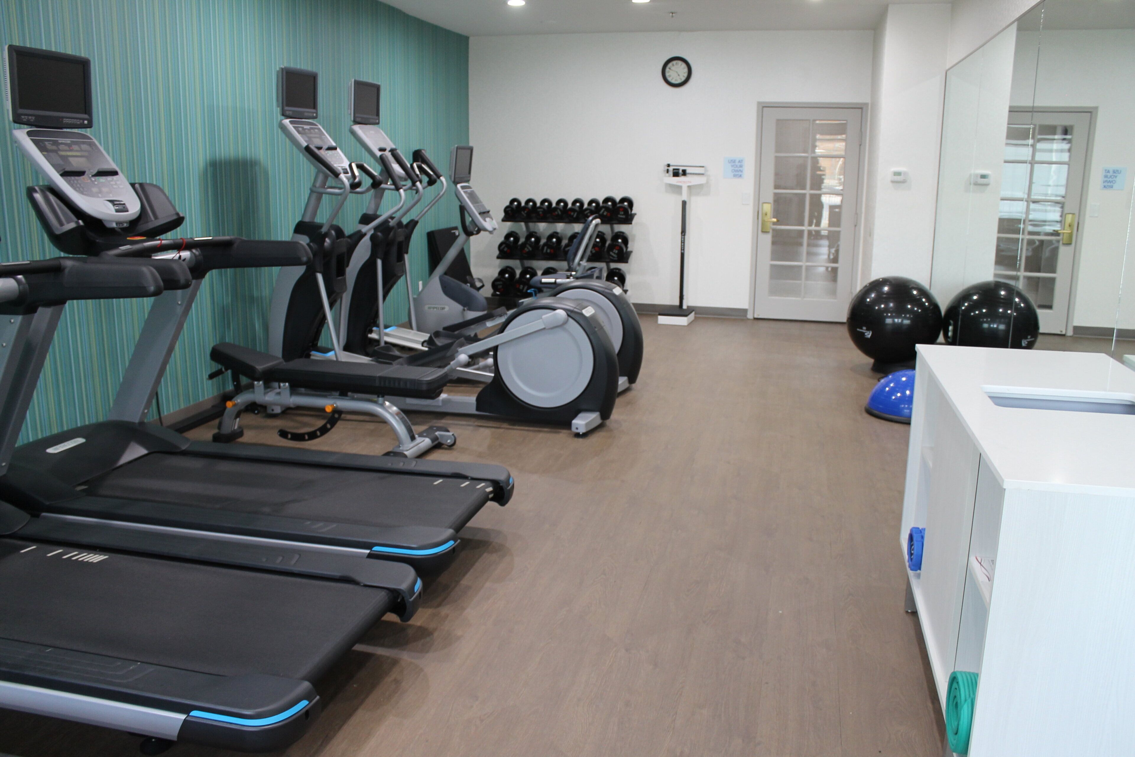 Un gimnasio con cintas de correr, bicicletas estáticas y pelotas de ejercicios.