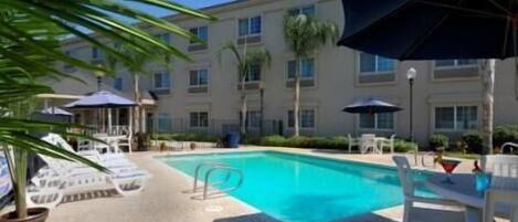 A hotel pool area with sun loungers, umbrellas, and a clear blue pool.