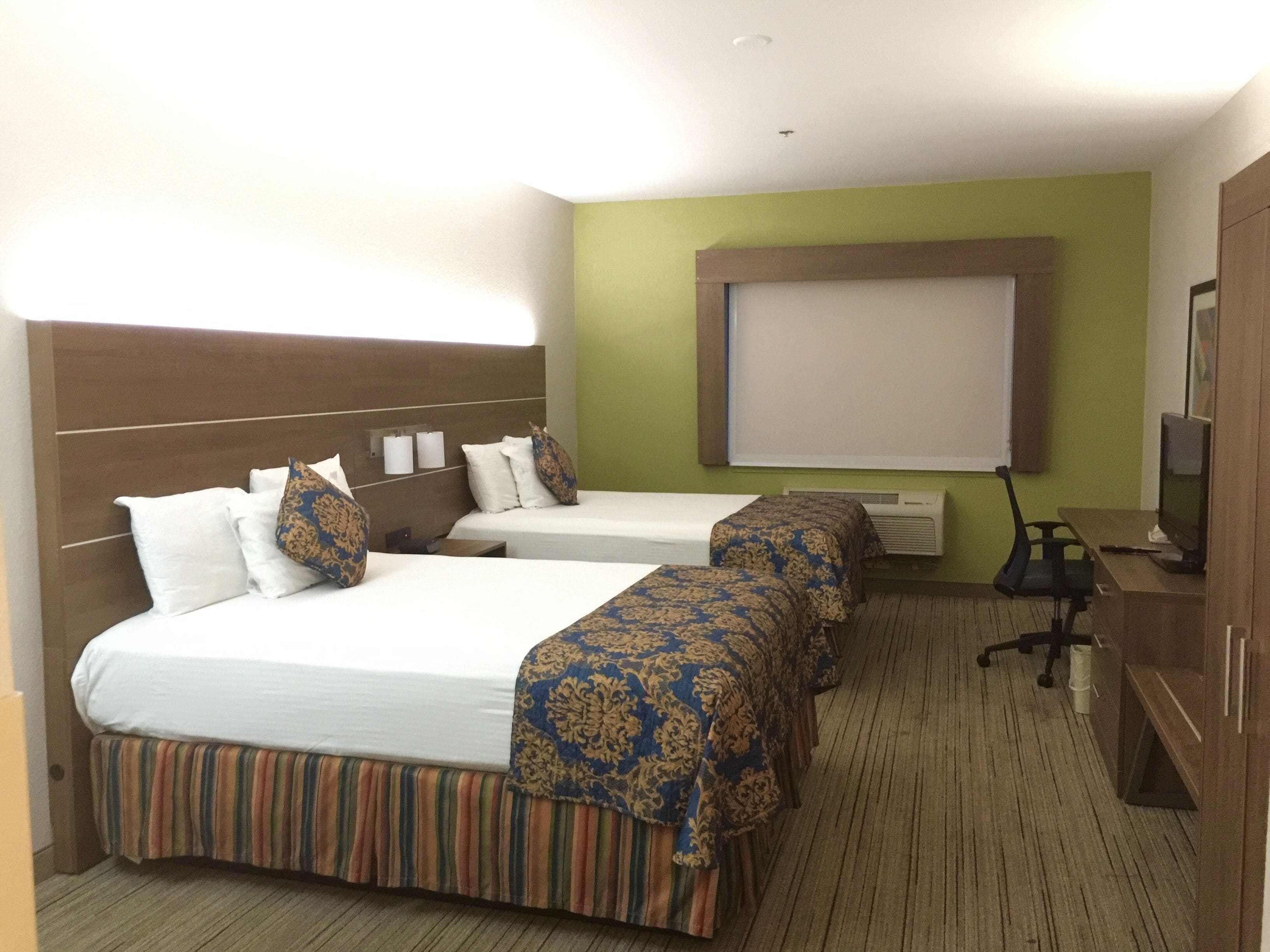 Habitación de hotel con dos camas, un televisor y una pantalla de proyector.