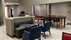 Uma área de refeições moderna com assentos em cabine, uma mesa redonda central e um bar com balcão e eletrodomésticos.