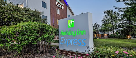 A Holiday Inn Express sign with a green logo, surrounded by greenery and flowers.