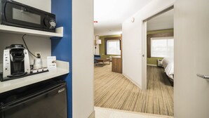 A hotel room with a kitchenette, a bed, a window, and a door leading to another room. - Holiday Inn Express Chicago NW - Vernon Hills by IHG (Vernon Hills)
