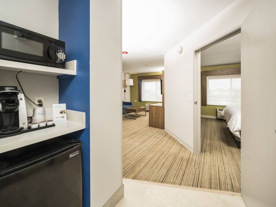 Ein Hotelzimmer mit Küchenzeile, einem Bett, einem Fenster und einer Tür zu einem weiteren Raum.