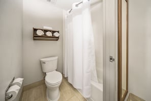 A bathroom with a toilet, a shelf with rolled towels, and a shower curtain. - Holiday Inn Express Chicago NW - Vernon Hills by IHG (Vernon Hills)
