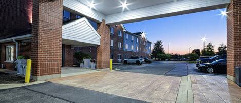 A parking area with a covered walkway leading to a building with multiple windows and a brick facade.