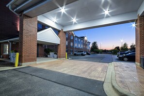 A parking area with a covered walkway leading to a building with multiple windows and a brick facade. - Holiday Inn Express Chicago NW - Vernon Hills by IHG (Vernon Hills)