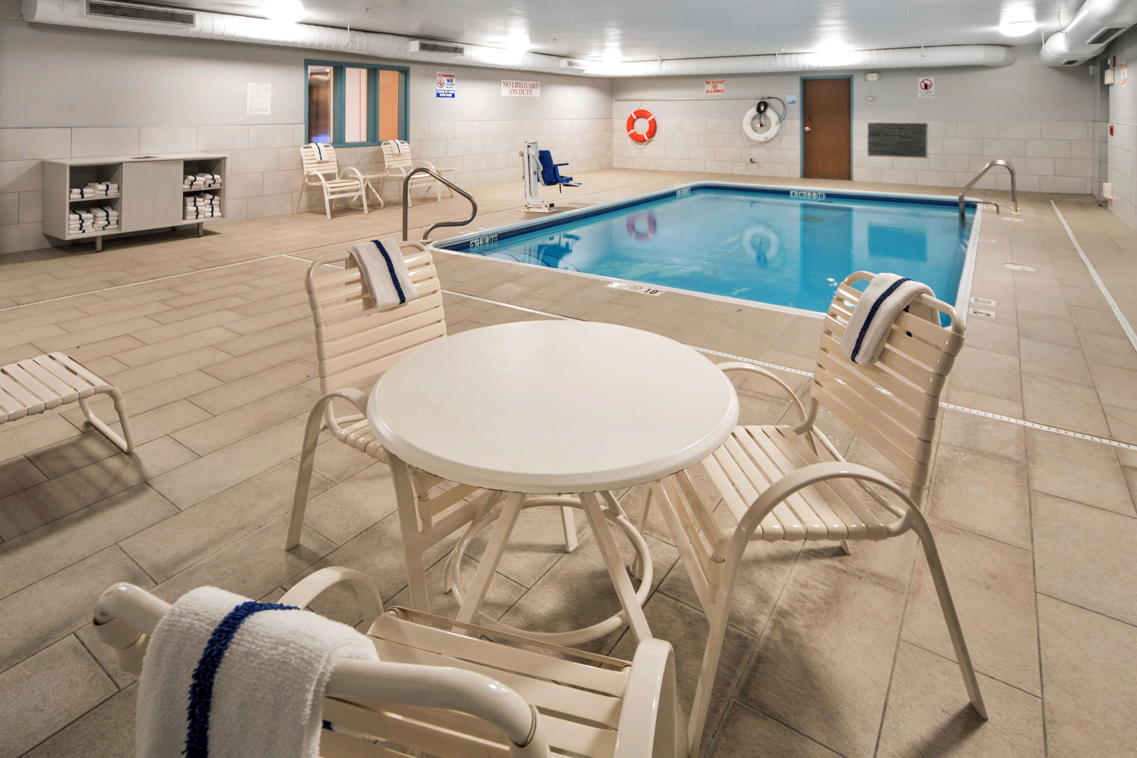 Zona de piscina interior con mesa de billar, sillas de descanso y un cartel de seguridad.