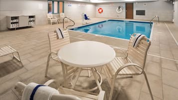 Zona de piscina interior con mesa de billar, sillas de descanso y un cartel de seguridad.
