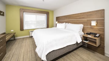 Habitación de hotel con una cama grande, una mesita de noche con lámpara, un escritorio pequeño y una ventana con vistas.