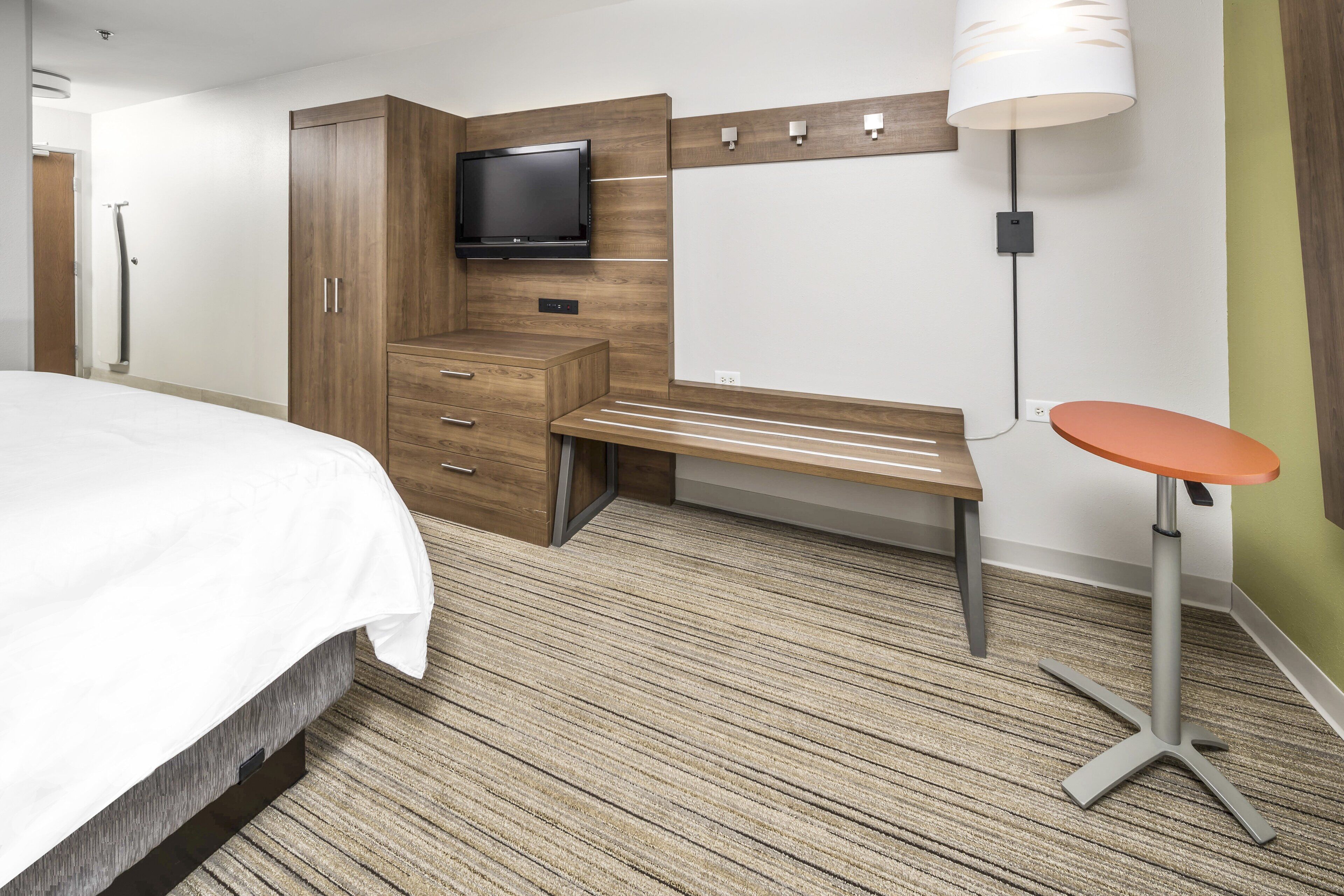 A hotel room with a bed, a desk, a television, and a lamp.