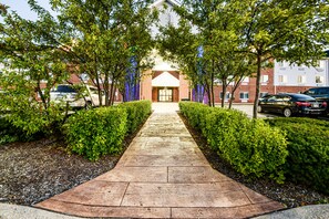 Un chemin pavé mène à un bâtiment dont la façade est en briques et qui possède une entrée centrale.