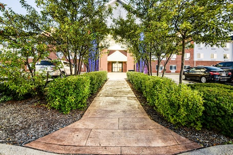 A paved pathway leading to a building with a brick facade and a central entrance.