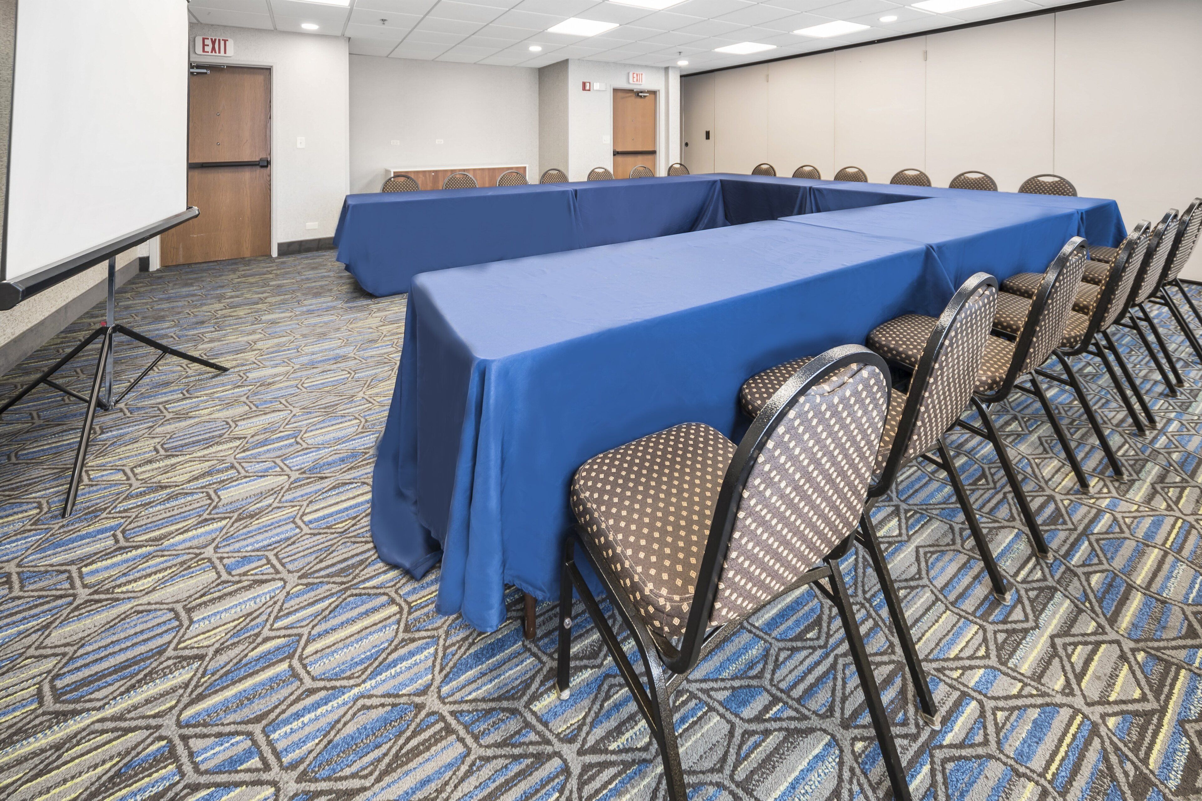 Une salle de conférence avec une longue table recouverte d’une nappe bleue, entourée de chaises au motif décoratif.