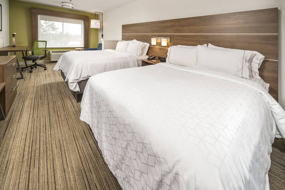 A hotel room with two beds, a desk, a chair, and a window.