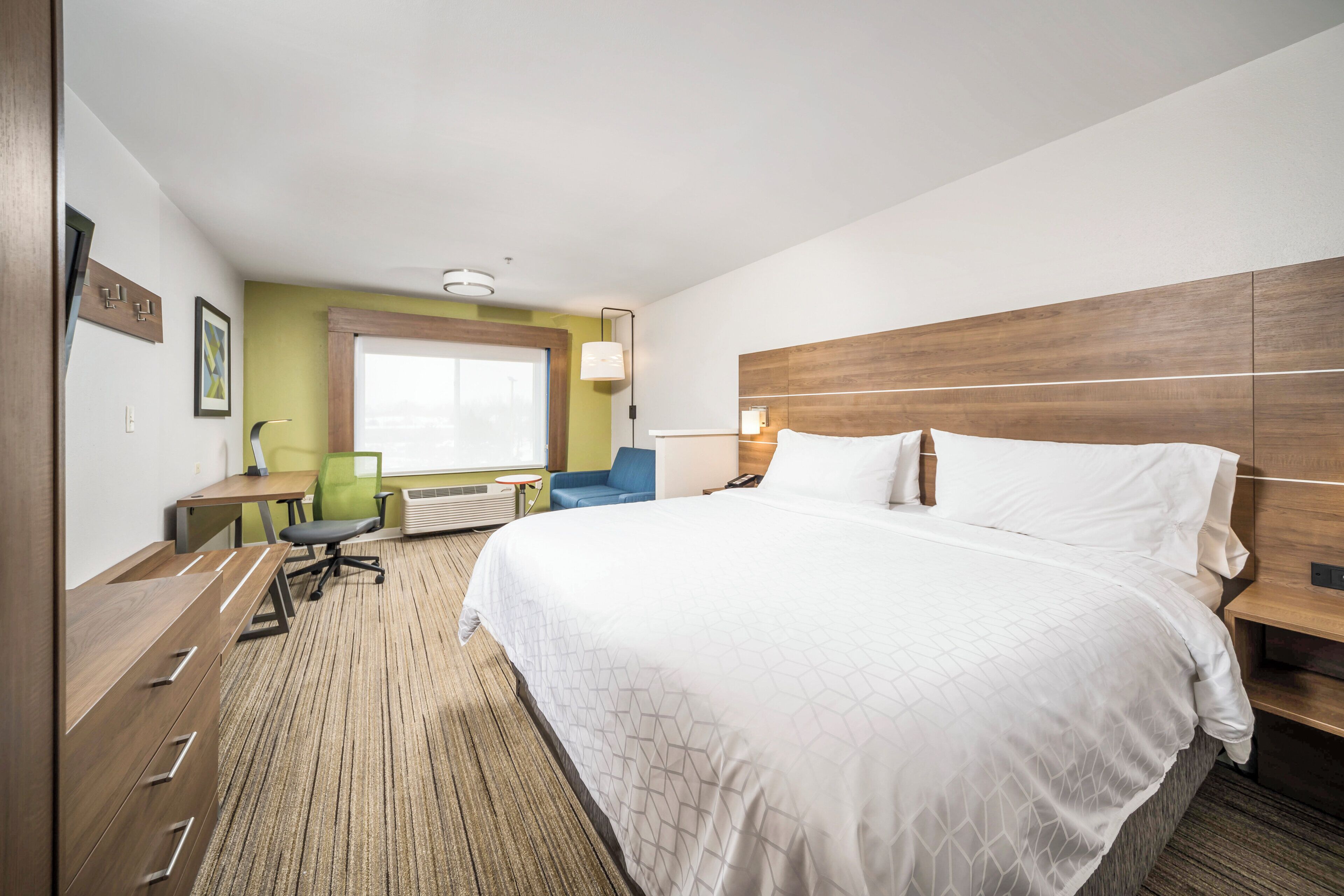 A hotel room with a large bed, a desk, a chair, and a window.