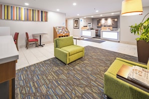 A lobby with a reception desk, a green armchair, a red chair, a small table, and a bookshelf. - Holiday Inn Express Chicago NW - Vernon Hills by IHG (Vernon Hills)