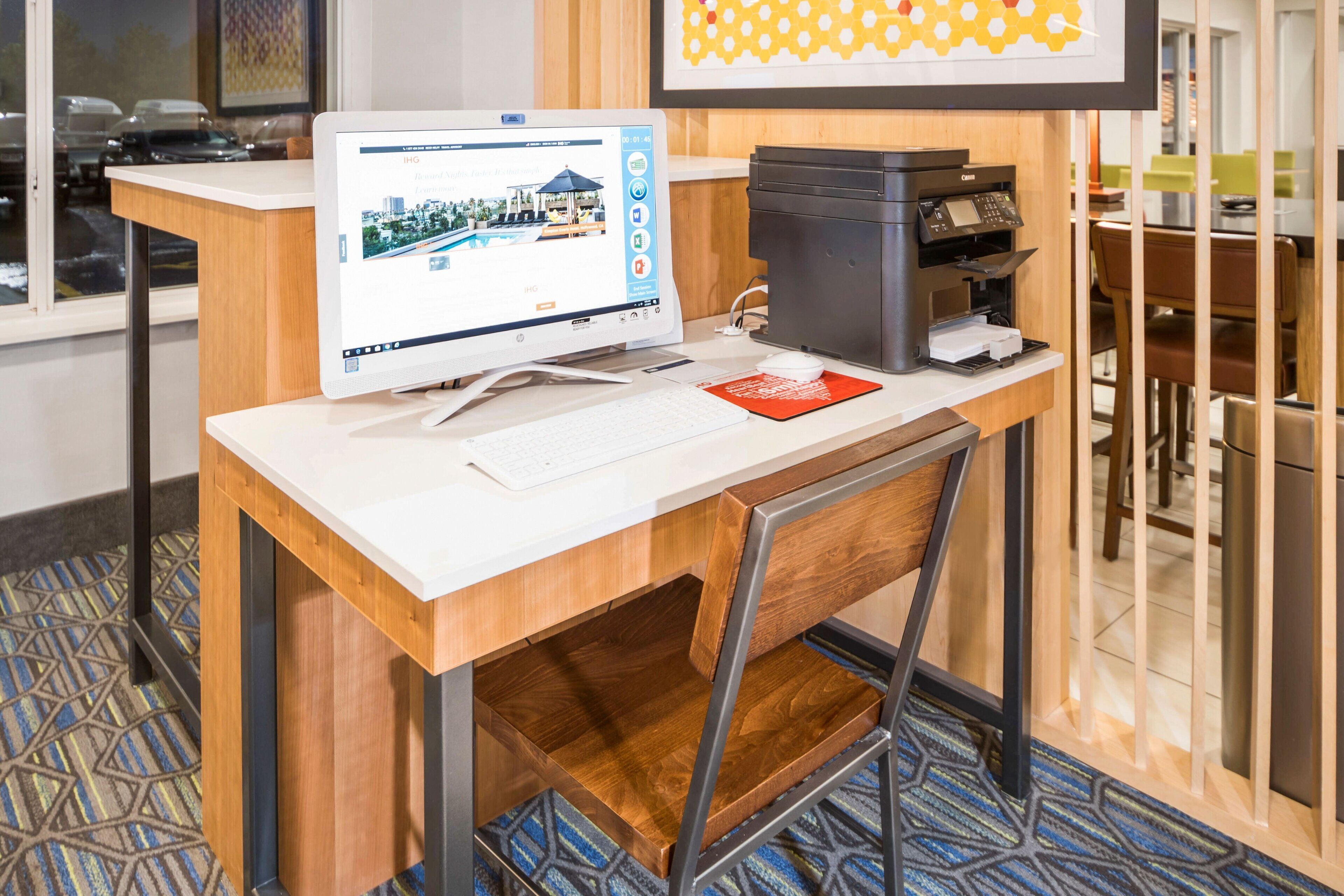 Un espacio de trabajo en un hotel con una computadora de escritorio, una impresora y un teclado sobre un escritorio.