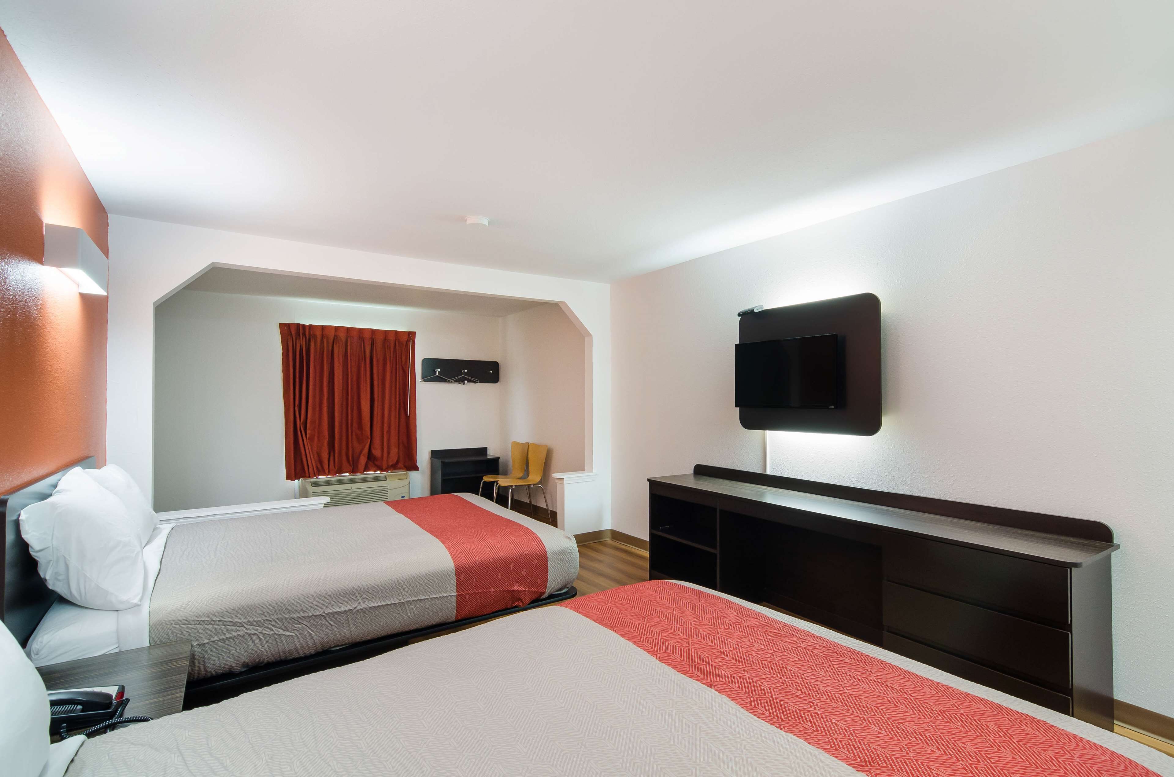 Habitación de hotel con dos camas, un televisor de pantalla plana montado en la pared, un escritorio y una silla.