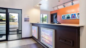 Zona de recepción de hotel con un diseño moderno, que incluye un mostrador de recepción, una puerta de cristal de entrada y una pared con cuadros enmarcados y un letrero.